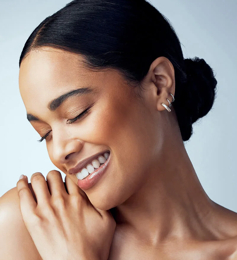Woman with her hair in a low bun and her hands resting near her collarbone