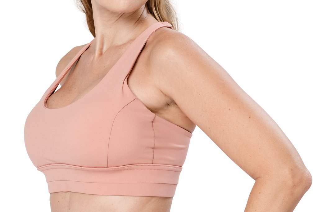 Side view of a woman in a pink sports bra, showing the upper fullness of the breast that an auto-augmentation breast lift aims to restore