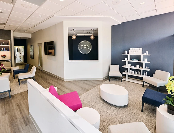 CPS office reception area with modern seating, white oval ottoman, pink accent pillow, dark blue wall with product shelving, and CPS logo signage